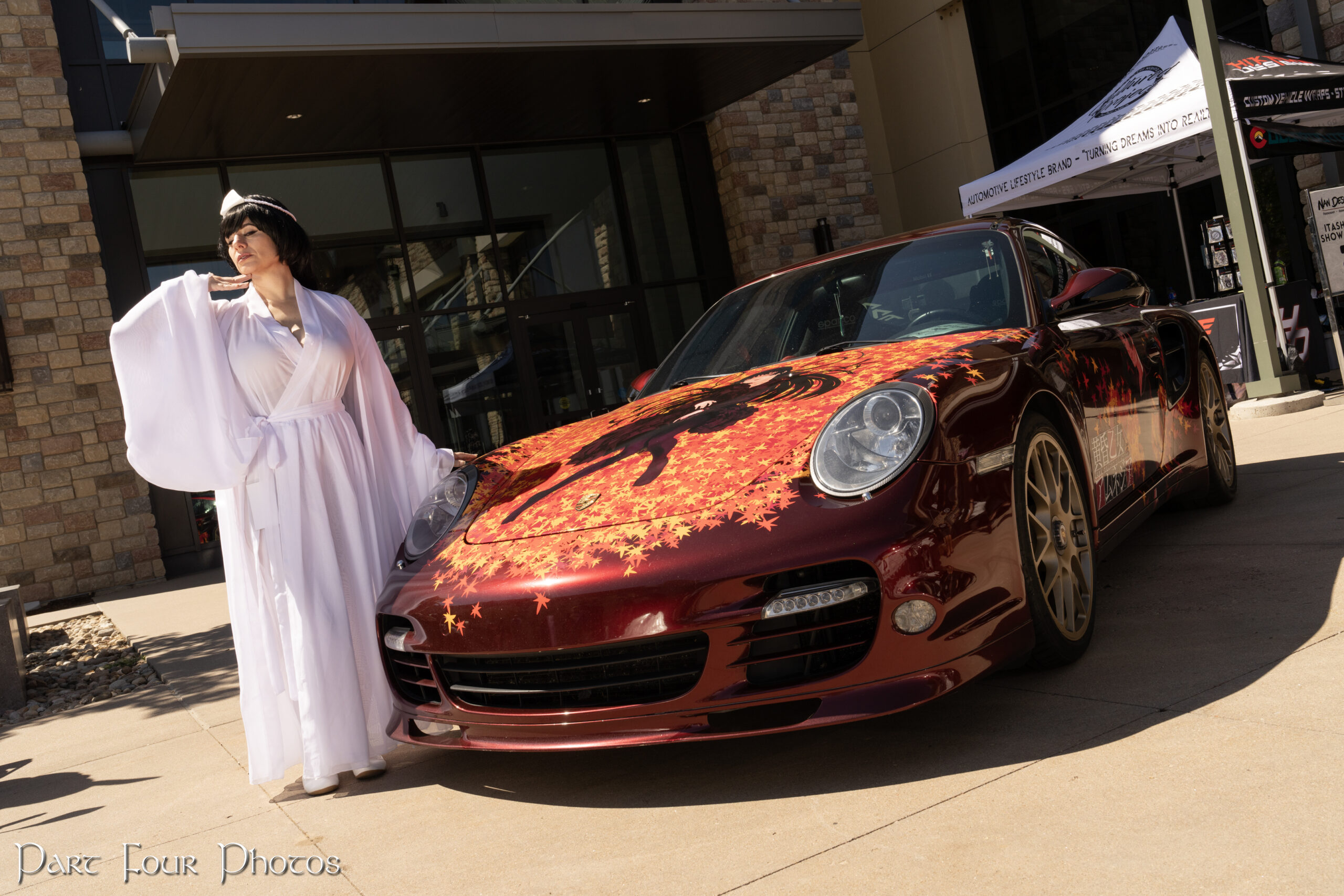 Itasha Porsche wrapped with a fall leaves motif and a costumed attendee standing near the front.